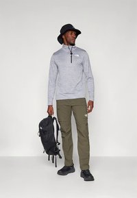 Siv pulover z dolgimi rokavi z zadrgo, olivno zelene hlače na vrečke, črna klobučasta kapa, črn nahrbtnik in črni superge.