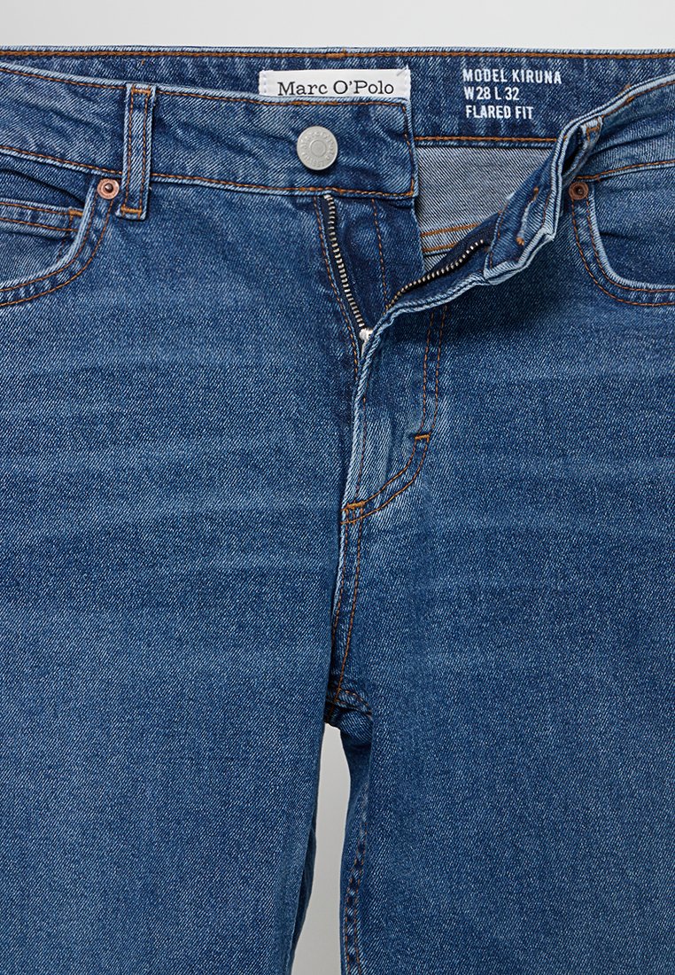 Blauwe spijkerbroek met gedeeltelijk open rits, metalen knoop, oranje stiksels en witte maatlabels aan de binnenkant van de tailleband.