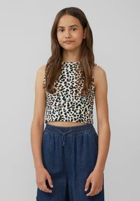 Ärmelloses Cropped Top aus einem beigen Stoff mit einem bunten Leopardenmuster. Kombiniert mit lockeren blauen Denim-Hosen mit einem elastischen Bund.