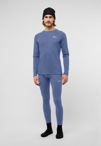 Blaues langärmliges Thermoshirt und enganliegende Leggings aus Stretchstoff. Mit Logo auf der Brust und kontrastierenden Nähten. Schwarze Socken.