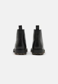 Botas de tobillo de cuero negro con una textura suave, suela de goma con patrones antideslizantes y lengüetas en la parte posterior para ponerlas y quitarlas fácilmente.