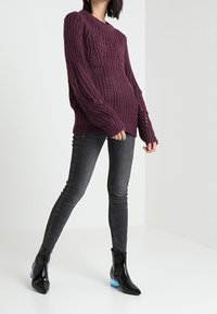 Maglione lavorato a maglia bordeaux con un motivo testurizzato, abbinato a jeans neri aderenti e stivali neri lucidi con tacco blu.