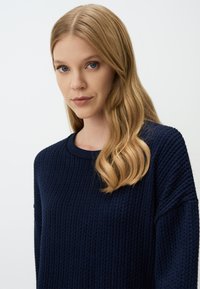 Dunkelblauer Strickpullover mit geripptem Muster, runder Ausschnitt und leicht überschnittenen Schultern.