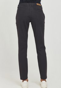 Črne, slim-fit hlače iz mehke bombažne tkanine, z rjavim blagovno znamko označenim pasom in zadnjim žepom. Noge se zožijo proti gležnjem.