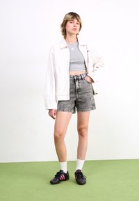 Atklāta balta pārmērīga krekla, pelēka īsa topa, augsto vidukļa melno džinsu šortu un melnu sporta apavu ar rozā akcentiem kombinācija.