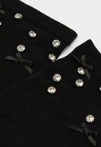 Czarna tkanina z małymi, okrągłymi cyrkoniami i czarnymi satynowymi kokardkami jako akcenty. Zbliżenie, teksturowana powierzchnia z błyszczącymi zdobieniami.