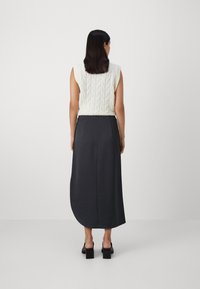 Krämfärgad stickad topp med mönstrad textur, kombinerad med en mörk, flödande långkjol. Svarta klackskor med blockklack fulländar outfitten.
