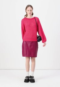 Un pull en maille épaisse de couleur rose vif avec des manches longues, associé à une jupe en cuir bourgogne ajustée. Un sac à bandoulière noir et des chaussures à plateforme complètent le look.