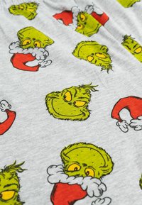 Tessuto grigio con volti di cartone animato del Grinch ripetuti, con pelle verde brillante, occhi gialli e cappelli di Babbo Natale rossi, contornati di nero.