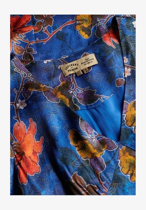Tissu à motifs bleus présentant des designs floraux en orange, jaune et violet. Comprend une étiquette visible avec la marque "SUPERDRY" et "PREMIUM".