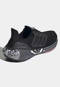 Scarpa sportiva nera con tomaia.texturizzata, dotata di tre strisce e suola decorata in varie sfumature di nero, bianco e dettagli rosa.