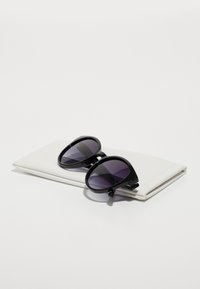 Ochelari de soare negri cu rame ovale și lentile violet cu gradient, așezați pe o husă albă pliată. Textură netedă cu detalii minime.