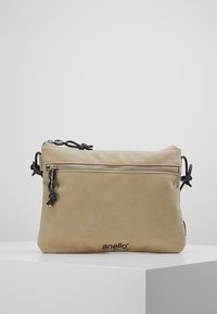 Beżowa torba na ramię wykonana z miękkiego materiału, z górnym zamkiem błyskawicznym, przednią kieszonką oraz regulowanymi czarnymi sznurkami. Logo wydrukowane z przodu.