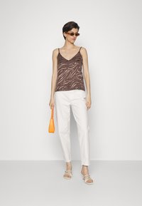 Camisola com padrão de zebra castanho e alças finas, combinada com calças brancas e sandálias com tiras. Os acessórios incluem uma pequena mala laranja.