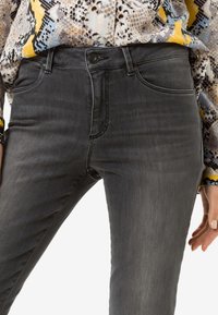 Jeans de mezclilla gris con un diseño ajustado, tiro medio, cinco bolsillos y costuras en contraste. El tejido parece ligeramente desgastado para un aspecto casual.