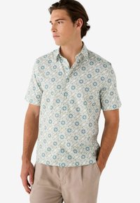 Camisa de botones de manga corta en verde claro con un estampado floral que presenta acentos en azul y blanco. Hecha de una tela ligera, tiene un ajuste holgado.