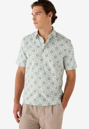 Camisa de botones de manga corta en verde claro con un estampado floral que presenta acentos en azul y blanco. Hecha de una tela ligera, tiene un ajuste holgado.