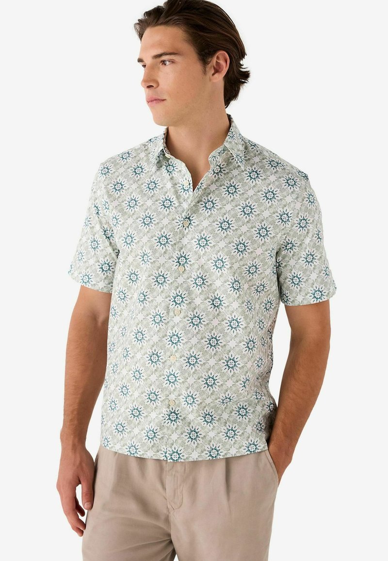 Camisa de botones de manga corta en verde claro con un estampado floral que presenta acentos en azul y blanco. Hecha de una tela ligera, tiene un ajuste holgado.