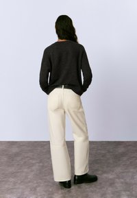 Sweater gris oscuro de corte relajado, pantalones de pierna ancha color crema con bolsillos traseros y botines negros. Texturas suaves, diseño minimalista.