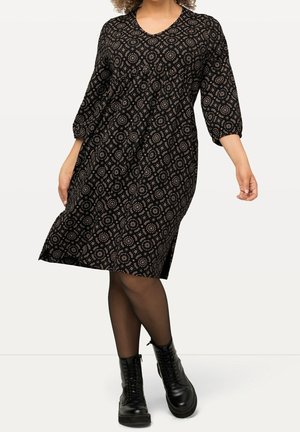 Czarna sukienka z trzema ćwierć rękawami, dekoltem w kształcie litery V i okrągłym wzorem. Lekka tkanina, długość do kolan, w połączeniu z czarnymi butami bojowymi.