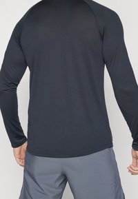 Długi rękaw, ciemnoszara sportowa koszulka wykonana z gładkiej, oddychającej tkaniny odprowadzającej wilgoć, wyposażona w zaokrąglony dół i rękawy raglanowe.