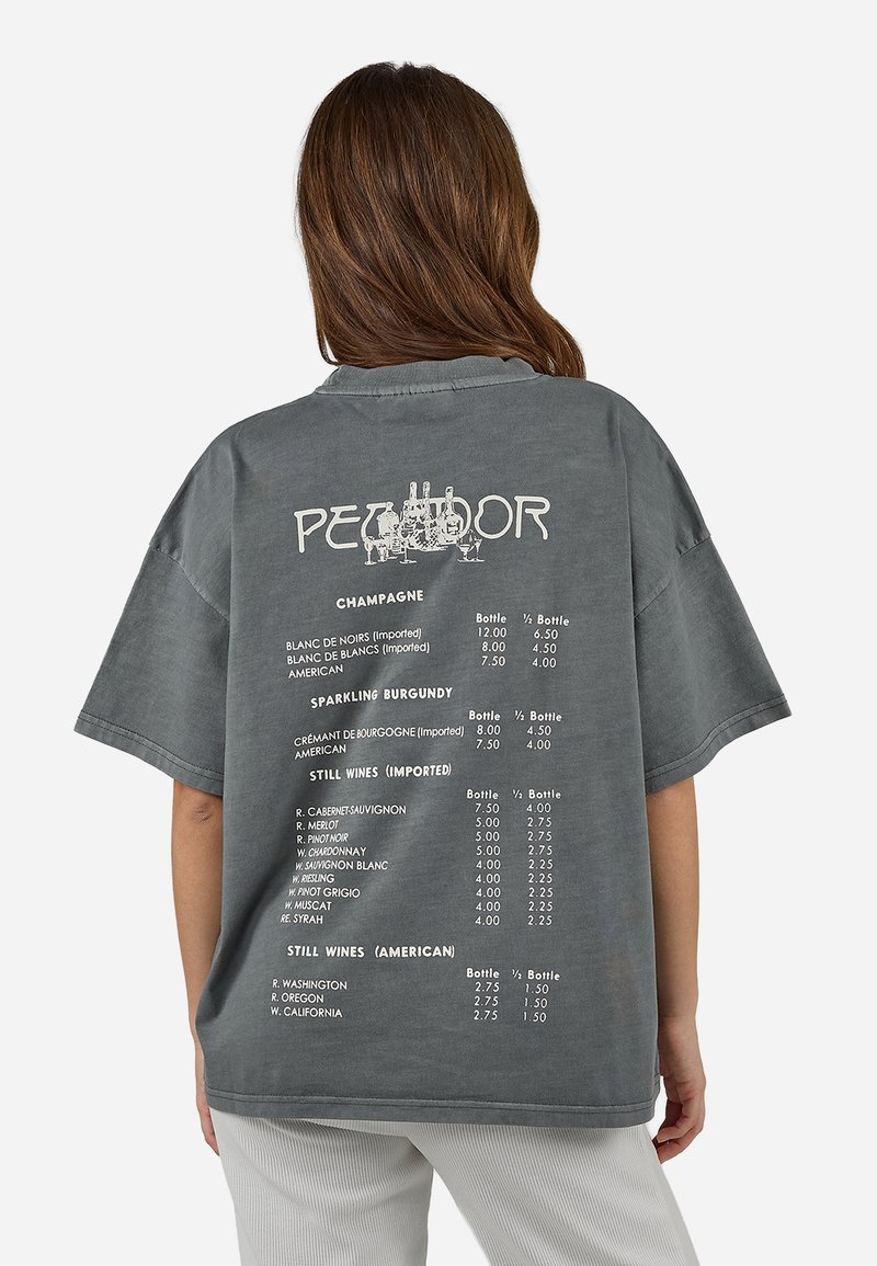 Άτομο με καστανά μαλλιά φοράει γκρι φαρδιά μπλούζα με λίστα τύπων κρασιού και τιμών, απεικονίζεται από πίσω μπροστά σε λευκό φόντο.