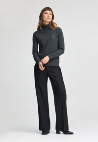 Pull col roulé gris foncé à manches longues, avec une texture lisse, associé à un pantalon large noir et des bottines à talons noires.