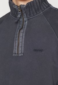 Pull-over demi-fermeture éclair en mélange de coton gris foncé, avec col côtelé, fermeture éclair contrastante et broderie discrète du logo sur la poitrine.