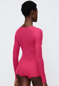 Langärmliges, figurbetontes Oberteil aus leuchtend pinkem Rippstoff, mit rundem Ausschnitt und nahtlosem Design. Kombiniert mit passender pinker Unterwäsche.