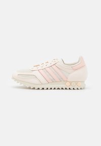 Lightweight athletic shoe in cream and pastel pink. Features synthetic and mesh upper, three diagonal stripes, and a textured rubber sole.