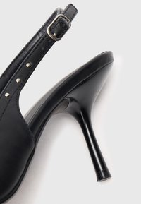 Melns ādas augstpapēžu sandalete ar pointētu purngalu, siksniņu ap papēdi ar sudraba sprādzi un dekoratīviem kniedēm gar siksniņu.