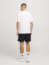 Camiseta deportiva blanca de mangas cortas con un acento reflectante en la parte trasera, combinada con pantalones cortos negros y zapatillas de deporte blancas.