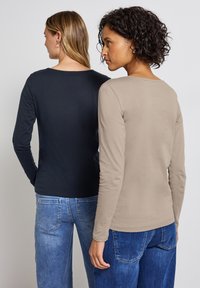 Två modeller som bär långärmade toppar: en i mörk marinblå, den andra i beige. Båda har rundade halslinjer och ett mjukt, lätt tyg.