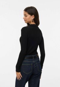 Svart ribbad långärmad topp med krage, tillsammans med högmidjade mörk denimjeans med ett svart bälte och synliga bakfickor.
