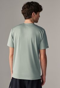 Camiseta deportiva de color verde claro con un acabado texturizado y cuello redondo. Mangas cortas y sin logos ni patrones visibles. Talla estándar.