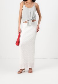Szaro-pasiasty top na ramiączkach z wiązaniem z przodu, zestawiony z białą, teksturowaną maxi spódnicą. Całość dopełnia czerwona torebka i jasnobrązowe sandały na obcasie z paskami.
