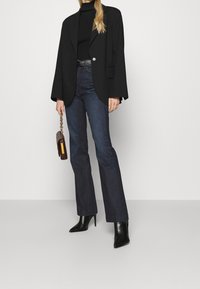 Svart oversized blazer, svart polokrage, mörkblå utsvängda jeans, svarta spetsiga ankelboots och en brun handväska med kedjerem.