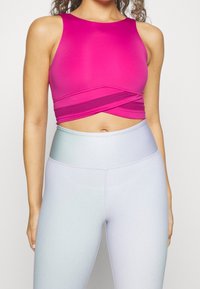 Přiléhavý krátký top v jasně růžové barvě s širokými ramínky a překříženým designem. Kombinováno s vysokým pasem, hladkými, světle modrými legínami.