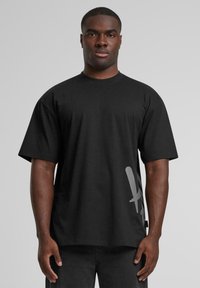 Black cotton t-shirt with short sleeves, featuring a large grey graphic on the side. Round neckline and relaxed fit, minimal texture.