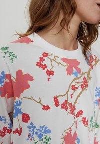 Blommönstrad sweatshirt med vit botten; pryds av färgglada rosa, blå och röda blommor samt gröna blad med en mjuk textur och rundad halsringning.