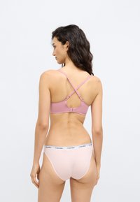 Ασύρματο σουτιέν σε απαλό ροζ με ρυθμιζόμενους σταυρωτούς ιμάντες και πίσω άνοιγμα με τρύπα. Συνδυαστικό ανοιχτό ροζ στρινγκ με λευκή ζώνη μέσης με λογότυπο.