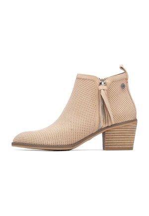 Bota beige al tobillo hecha de ante perforado, con cremallera lateral, detalle de borla y tacón apilado. Presenta un diseño de punta redondeada y lisa.