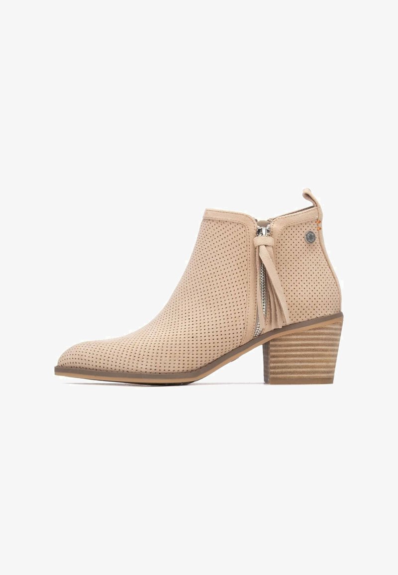 Bota beige al tobillo hecha de ante perforado, con cremallera lateral, detalle de borla y tacón apilado. Presenta un diseño de punta redondeada y lisa.