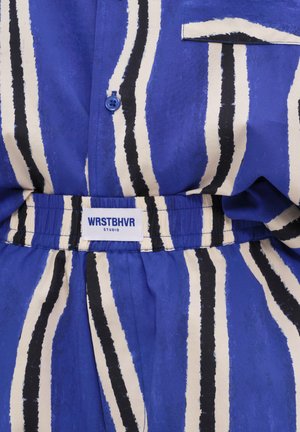 Blau-weiß vertikal gestreifter Stoff mit einem Knopf und einem elastischen Bund mit der Aufschrift „WRSTBHVR STUDIO.“