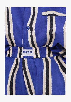 Blau-weiß vertikal gestreifter Stoff mit einem Knopf und einem elastischen Bund mit der Aufschrift „WRSTBHVR STUDIO.“