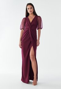 Burgundijas vakara kleita ar pagrieztu priekšpusi, caurspīdīgām puff piedurknēm un augstu šķiršanos, izgatavota no gludas auduma ar mīkstu tekstūru.