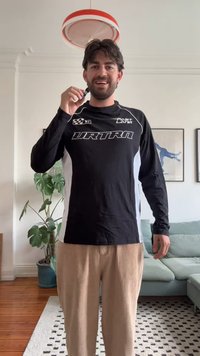 Musthave mustagaheline mustroheline t-särk hallide aktsentidega, millel on valge logo ja ruuduline disain. Kandmine beežide puuvillaste pükstega. Siseruumides.
