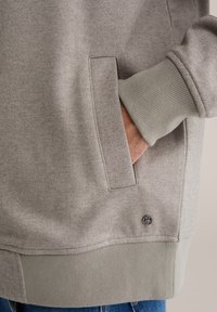 Hall hallharinguriga dressipluus, millel on soonikust mansett ja alumineäär, küljetasku detail ning väike logo accent alumisel äärisel.