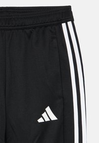 Schwarze Sporthose mit weißen Seitenstreifen und einem weißen Logo. Der Stoff hat eine strukturierte Oberfläche und einen elastischen Bund.