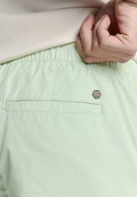 Lichtgroene shorts met een elastische tailleband, met een achterzak en een klein hexagonaal logo accent nabij de zak. Glad textuur.